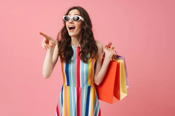 Beautiful pleased positive happy young cute woman posing isolated over pink wall background holding shopping bags. — Stock Photo, Image