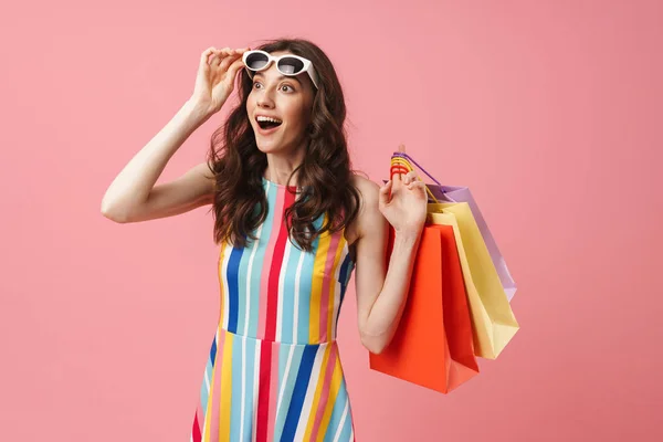 Gyönyörű örömmel pozitív boldog fiatal csinos nő jelentő elszigetelt több mint rózsaszín fal háttér gazdaság bevásárló táskák. — Stock Fotó