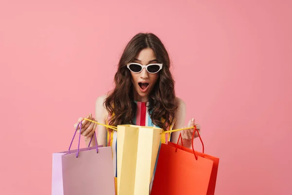 Gyönyörű örömmel pozitív boldog fiatal csinos nő jelentő elszigetelt több mint rózsaszín fal háttér gazdaság bevásárló táskák. — Stock Fotó