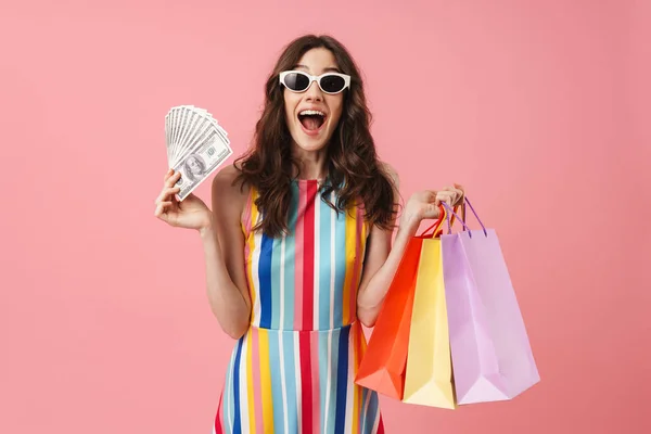 Beautiful happy positive young young cute woman posing isolated over pink wall background holding shopping bags . — Stok Foto