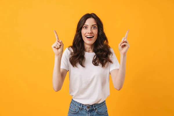 Emotional happy surprised young woman posing isolated over yellow wall background pointing. — Stockfoto