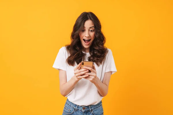 Glücklich schockiert emotionale junge Frau posiert isoliert über gelben Wand Hintergrund mit Handy. — Stockfoto