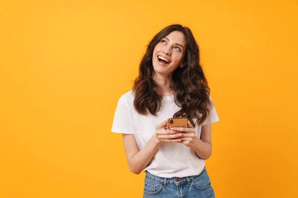 S radostí usmívající se mladá žena, která se izoluje nad žlutou stěnou pozadí pomocí mobilního telefonu. — Stock fotografie