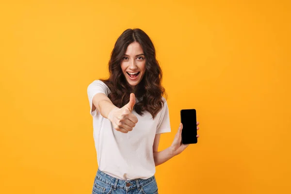 Boldog pozitív mosolygó fiatal nő pózol elszigetelt sárga fal háttér segítségével mobil telefon mutatja kijelző és remek. — Stock Fotó
