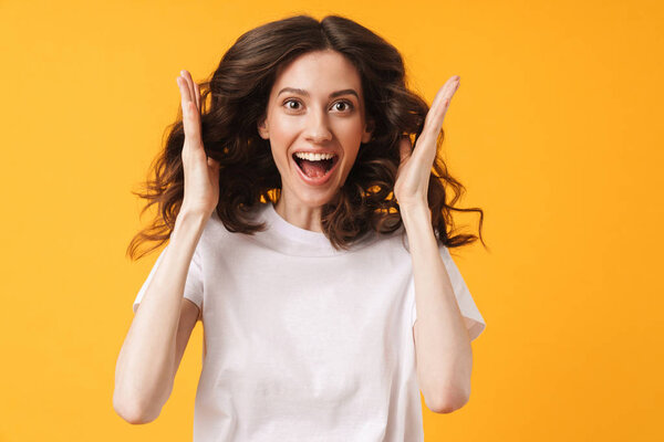 Шокированная эмоциональная улыбающаяся молодая женщина позирует изолированно на фоне желтой стены
.