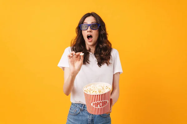 Bang geschokt jonge vrouw poseren geïsoleerd over gele muur achtergrond eten popcorn horloge film. — Stockfoto