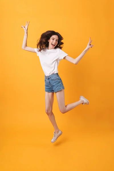 Emocjonalna młoda kobieta skoki na białym tle na żółto ściana pokazując spokój. — Zdjęcie stockowe