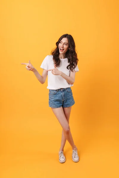 Mujer joven feliz posando aislado sobre fondo amarillo de la pared que apunta al espacio de copia . —  Fotos de Stock