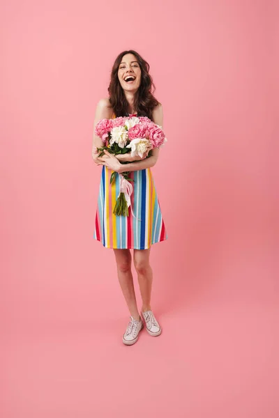 Feliz alegre sonriente joven linda mujer posando aislado sobre fondo de pared rosa sosteniendo flores . — Foto de Stock