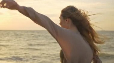 Heyecanlı, genç ve güzel bir kadın. Uçan saçları etrafında dönüyor ve deniz kenarında yürürken esintinin tadını çıkarıyor.