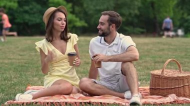 Parkta piknik yaparken ekose üzerinde oturup sohbet eden mutlu genç çift.