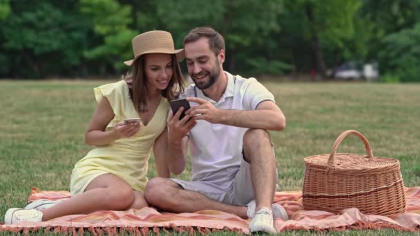 公園でピクニックをしながら スマートフォンを使って座って遊ぶ美しい若い素敵なカップル — ストック動画