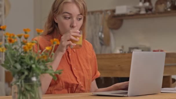 集中若いですブロンド女性仕事上のラップトップと飲み物ジュース中にザ キッチン — ストック動画