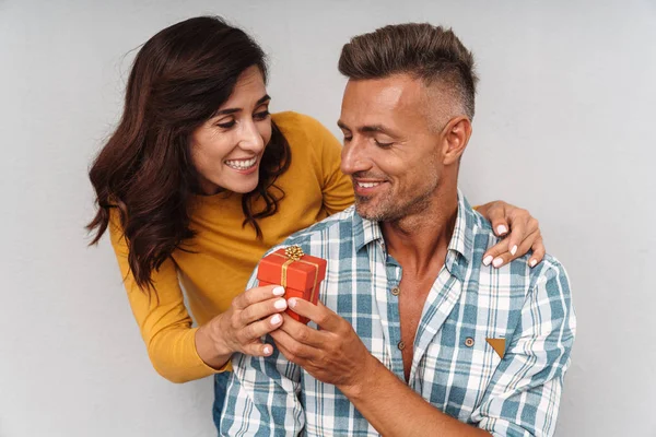 Fröhliche, fröhliche Frau schenkt ihrem Mann vor grauem Hintergrund ein Geschenk. — Stockfoto