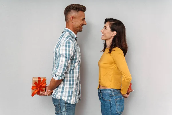 Niedlich optimistisch erwachsene liebende Paar isoliert über graue Wand Hintergrund halten Geschenke für einander. — Stockfoto