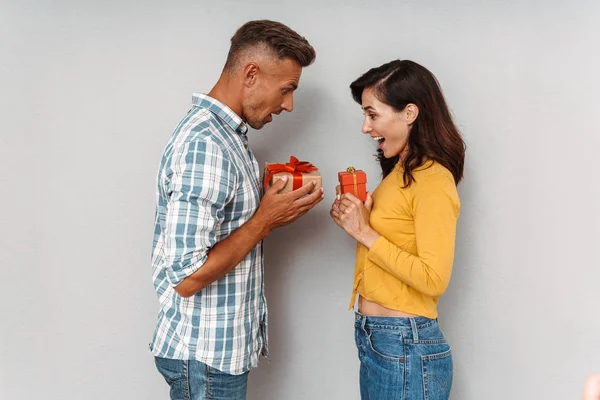 Χαριτωμένο αισιόδοξος ενήλικος στοργικό ζευγάρι απομονωθεί πάνω από γκρι τοίχο φόντο κρατώντας δώρα για το άλλο. — Φωτογραφία Αρχείου