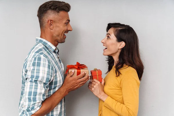 Linda pareja adulta optimista amorosa aislada sobre fondo de pared gris sosteniendo regalos el uno para el otro . — Foto de Stock