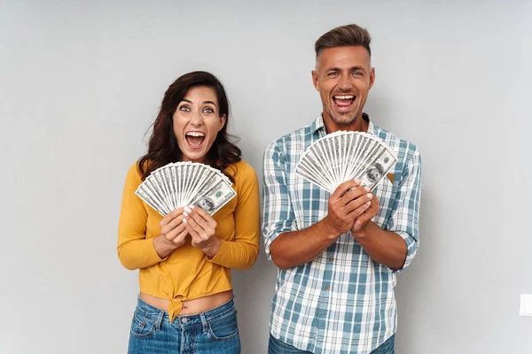 Emotional adult loving couple holding money isolated over grey wall background.