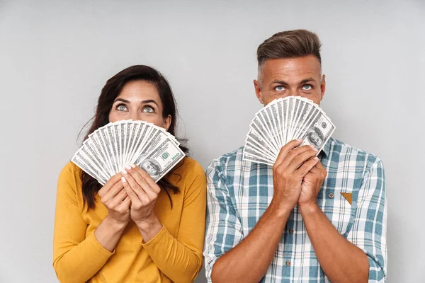 Emotional adult loving couple holding money isolated over grey wall background covering face. — Stock Photo, Image