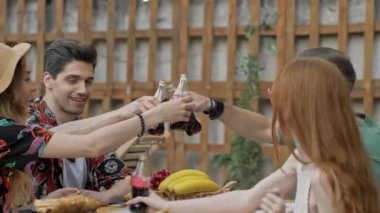 Bir grup mutlu genç arkadaş piknikte birlikte eğlenirken soda şişeleriyle tezahürat yapıyorlar ve içiyorlar.