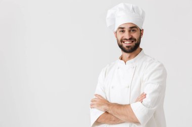 Genç aşçı üniformalı beyaz duvar arkasında yalnız poz veriyor..