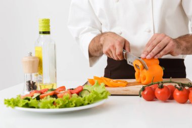 Üniformalı genç aşçının sebze keserken çekilmiş görüntüsü.