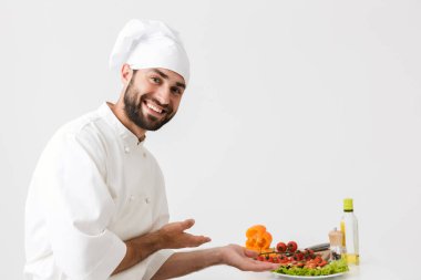 Aşçı şapkalı, gülümseyen ve vejeteryanla poz veren mutlu aşçı imajı.