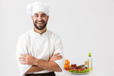 Aşçı şapkalı yakışıklı bir şef resmi. Gülümsüyor ve V ile poz veriyor.