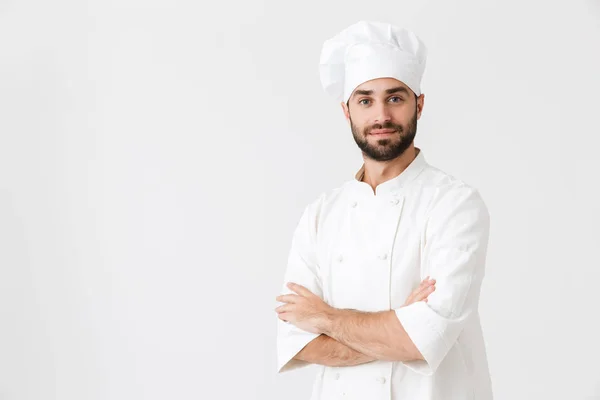 Concentrat tânăr bucătar care prezintă izolat pe fundal de perete alb în uniformă . — Fotografie, imagine de stoc