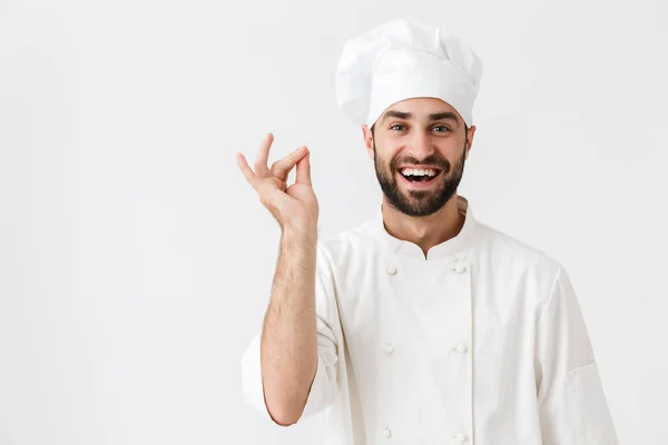 Alegre feliz jovem chef posando isolado sobre fundo parede branca em uniforme . — Fotografia de Stock