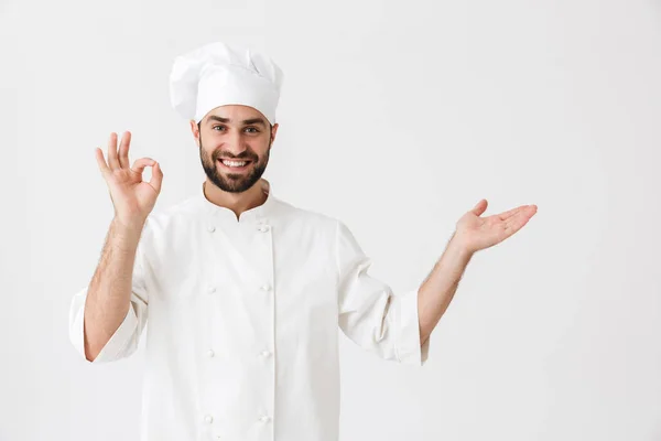 Gelukkige jonge chef poseren geïsoleerd over witte muur achtergrond in uniform maken oke gebaar tonen copyspace. — Stockfoto