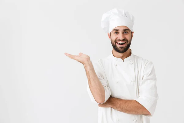 Jovem chef feliz posando isolado sobre fundo da parede branca em uniforme mostrando copyspace . — Fotografia de Stock