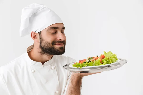 Image of pleased chief man in cook uniform smelling dish while h — Stock Photo, Image
