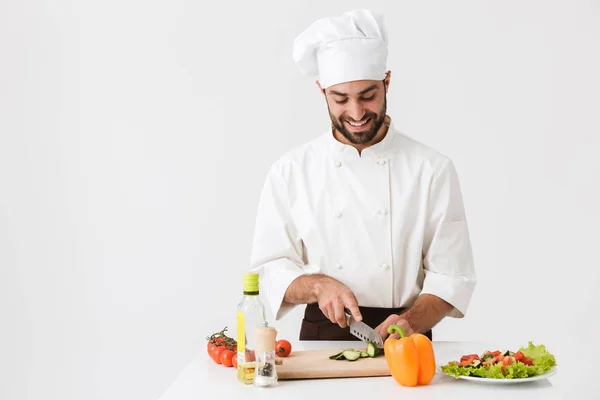 A boldog főnök képe egyenruhában, mosolyog és zöldséget főz. — Stock Fotó