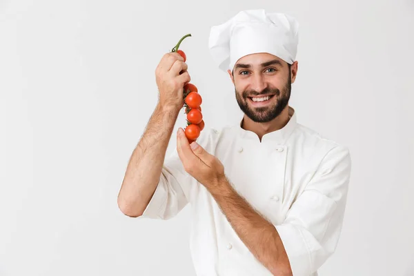 Imagem de homem chefe alegre em uniforme segurando tomates enquanto cozinheiro — Fotografia de Stock