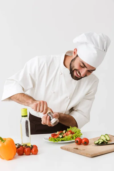 Erfreut positive glücklich junger Koch isoliert über weiße Wand Hintergrund in einheitlichen Kochen mit frischem Gemüse. — Stockfoto