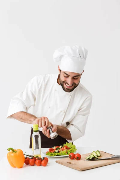 Agréable positif heureux jeune chef isolé sur fond de mur blanc en cuisine uniforme avec des légumes frais . — Photo