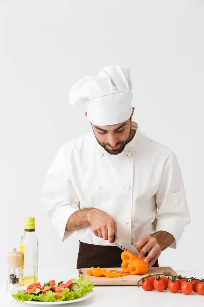 Image of optimistic cook man in uniform smiling and cutting vege — Stock Photo, Image