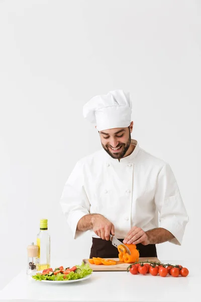 Imagem de homem cozinheiro satisfeito em uniforme sorrindo e cortando vegetab — Fotografia de Stock