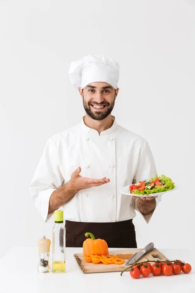 Bild eines kaukasischen Kochs in Uniform, der lächelt und Teller hält — Stockfoto