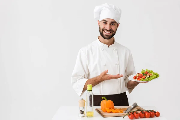 Bild von positivem Koch in Uniform, der lächelt und Teller hält — Stockfoto