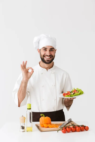 Bild av ung kock man i uniform visar ok tecken och innehav p — Stockfoto