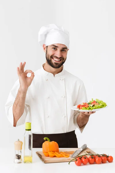 Imagem de homem cozinheiro bonito em uniforme mostrando delicioso sinal e — Fotografia de Stock