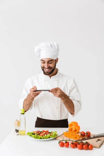 Imagem de homem cozinheiro feliz em uniforme sorrindo e tirando foto de p — Fotografia de Stock