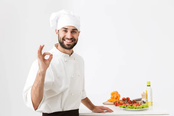 Obrázek šťastný kuchař muž v kuchař klobouk s úsměvem a ukazující lahůdku — Stock fotografie