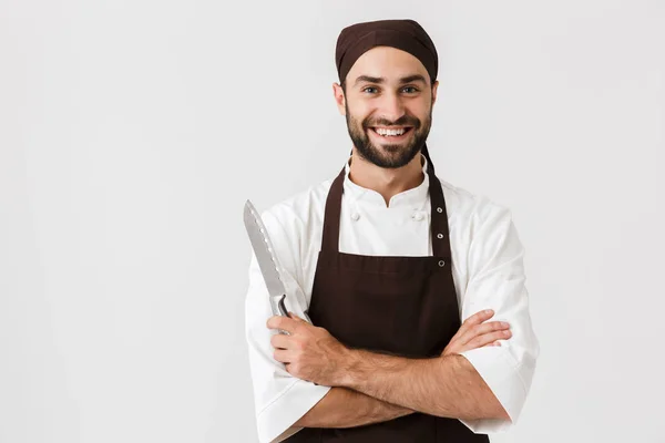 Joyeux sourire optimiste jeune chef su posant isolé sur fond de mur blanc en uniforme couteau de maintien . — Photo