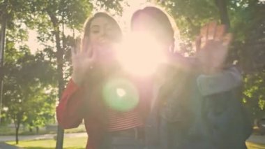 Mutlu genç kızlar. Parkta otururken gülümseyen ve kameraya el sallayan arkadaşlar.