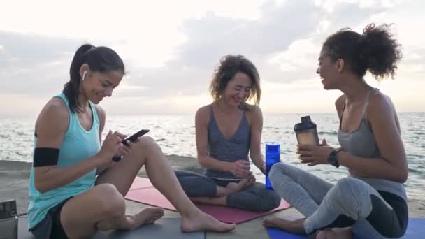 一群年轻美丽 多民族的女运动员朋友 一边在海滩边一边一边看智能手机上的东西 一边满脸笑容地说话 — 图库视频影像