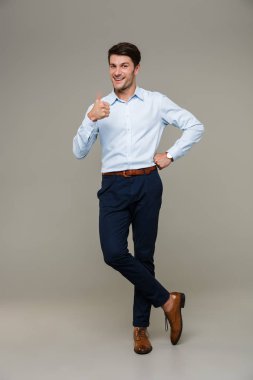 Resmi kıyafetler giyen, kameraya gülümseyen ve baş parmağını gösteren neşeli bir genç resmi.