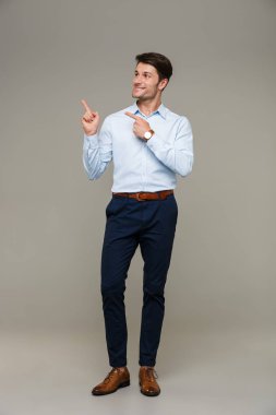 Resmi giysiler giymiş neşeli bir genç adam resmi. Gülümseyen ve parmaklarını kopyasal boşluğu işaret eden.